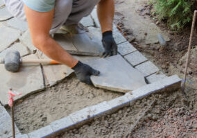 Construction of pavement near the house. Bricklayer places concrete paving stone blocks for building up a